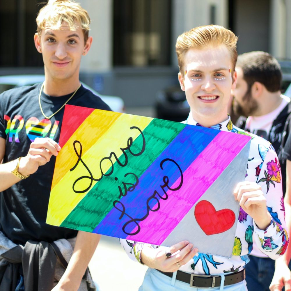 zwei Personen halten bunt gestreiftes Schild hoch "Love is Love"